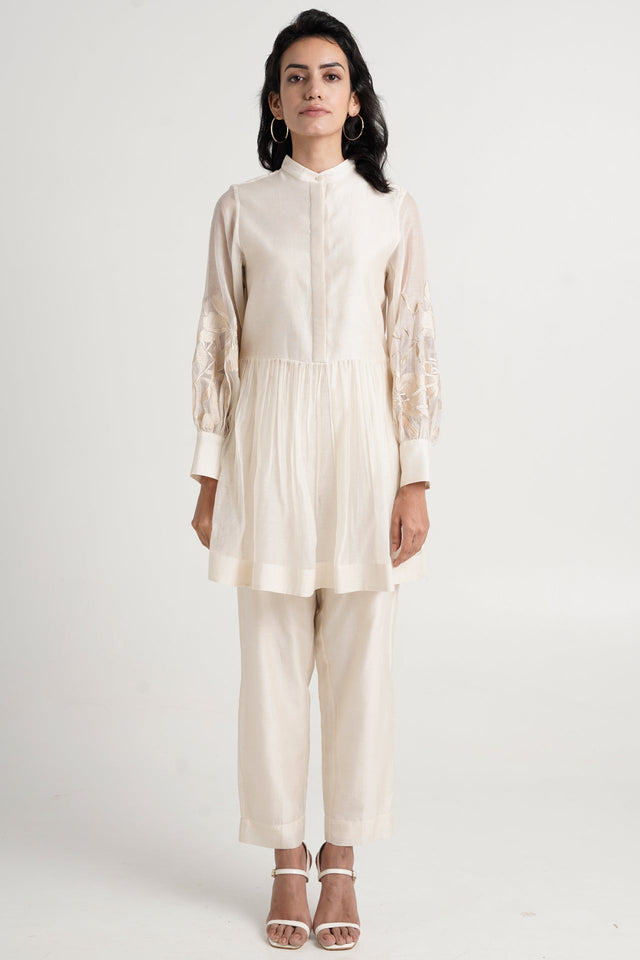 Ivory Abe 2.0 peplum tunic and slim pants with white heels, full length front view