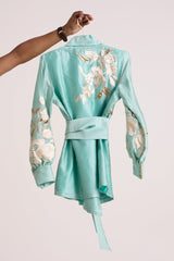 Aqua Alfie blazer top on a hanger, back view showing the obi belt and ivory floral applique