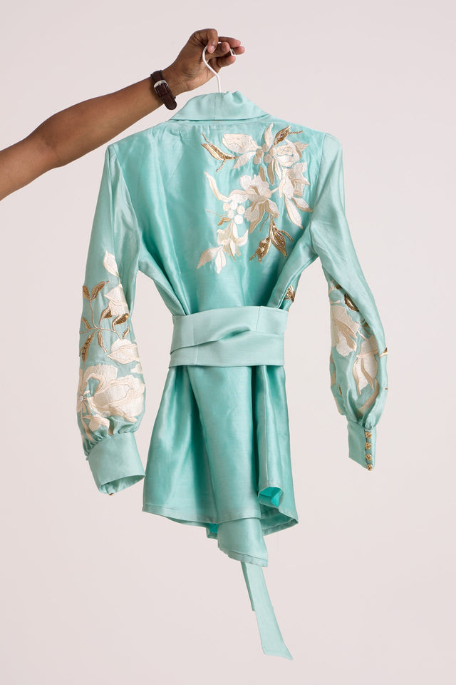 Aqua Alfie blazer top on a hanger, back view showing the obi belt and ivory floral applique