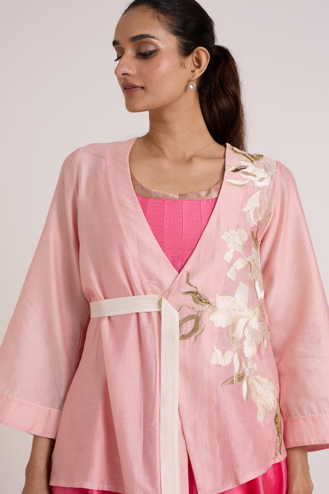 Close front view of the Hira-Jun blush overlap jacket with ivory belt and floral applique