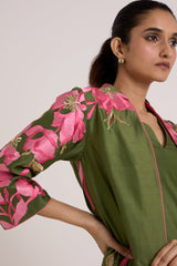 Close view of the Rafiya olive jacket sleeve with pink floral applique and a hand on the hip