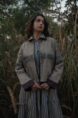 Model wearing the taupe Dune Pleated Jacket over a striped dress, front view outdoors