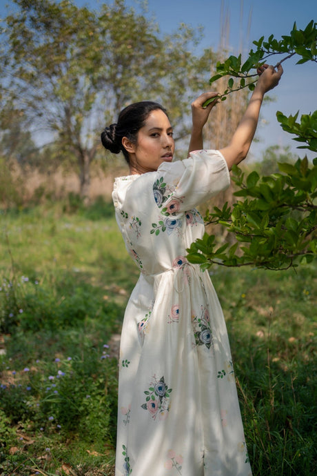 Ivory Drawstring dress with puff sleeves and floral print, model reaching up to a branch, side view