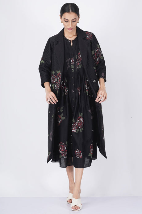 Model wearing the rose print jacket open over the pleated dress, looking down, front view
